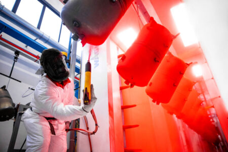 Un operatore vernicia a polvere rossa dei serbatoi in prossimità di una delle nostre cabine di verniciatura automatiche