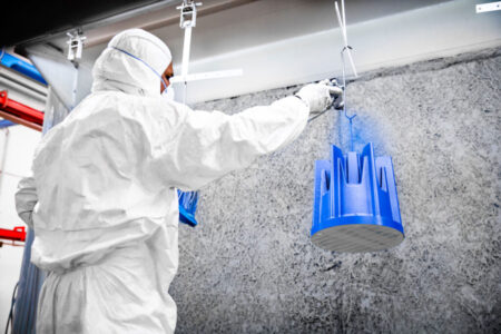 Un operatore vernicia a liquido blu un articolo all'interno di uno dei nostri impianti di verniciatura pressurizzati